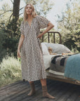 The Smocked Sleep Dress with brown bear print worn by a woman beside a metal bed frame in an outdoor setting.
