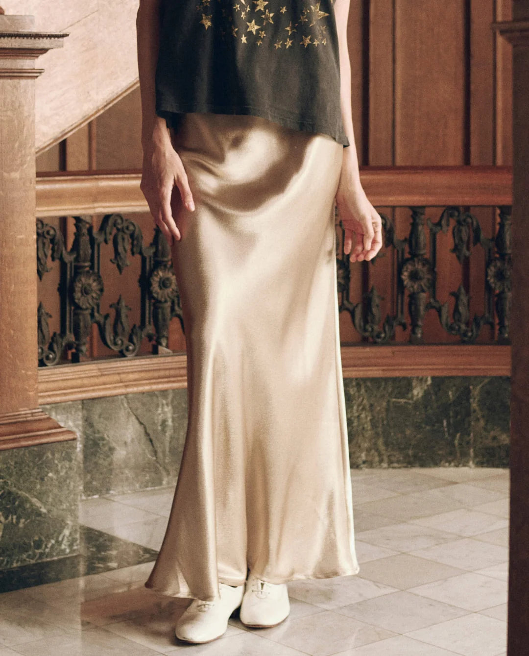 The Elastic Bias Skirt in gold, worn with a black top and white shoes.