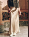 The Elastic Bias Skirt in gold, worn with a black top and white shoes.