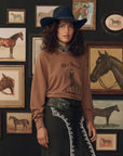 The Great Inc. College Sweatshirt with Stetson graphic, worn with a hat, in an equestrian-inspired art setting.