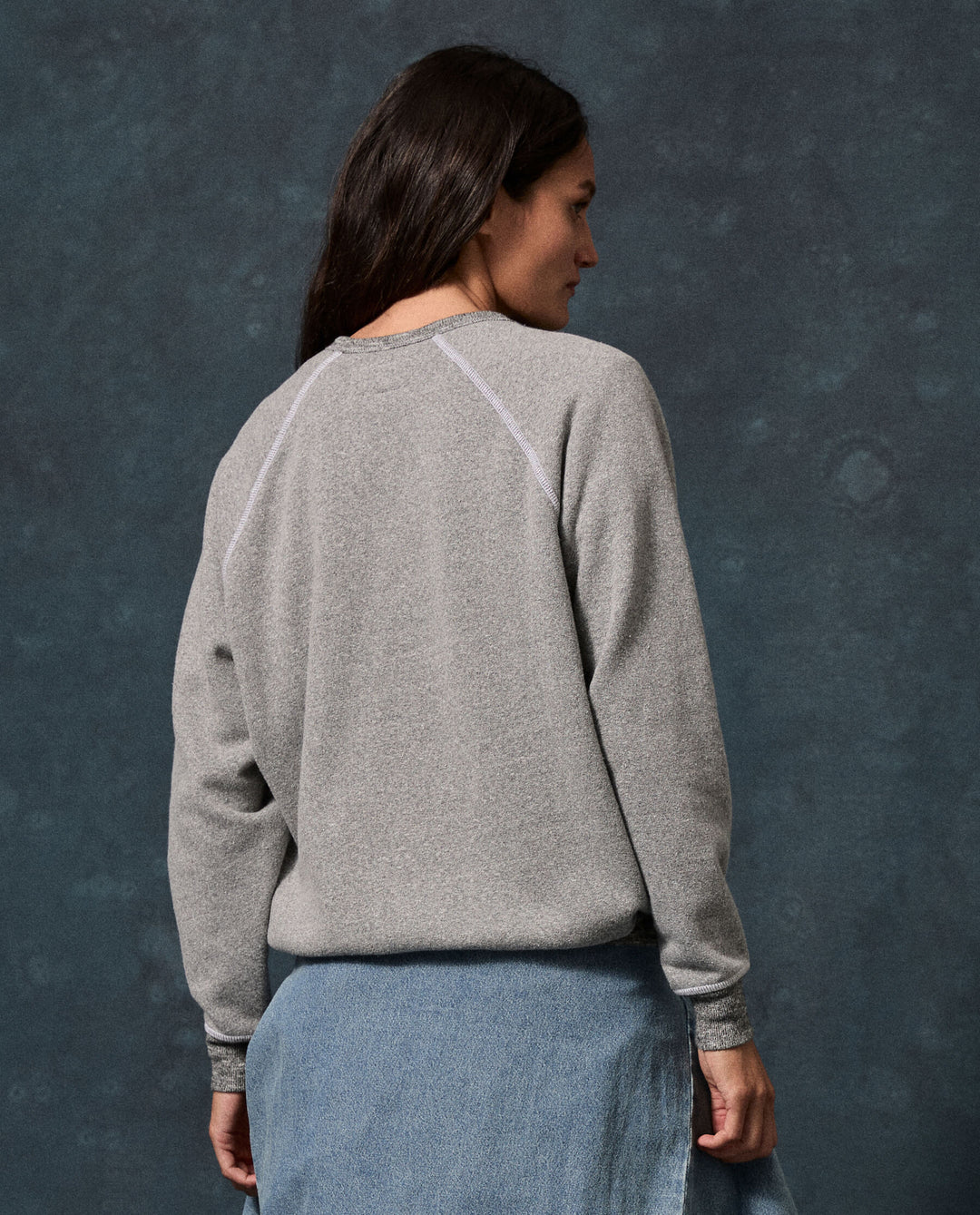 The Fleece College Sweatshirt by The Great Inc. styled with a denim skirt, model turned away.