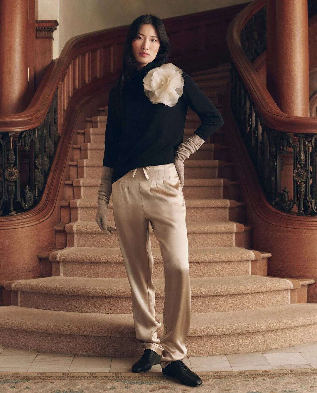 The Rayon Jersey Turtleneck with a large fabric flower worn with light trousers on a curved staircase.