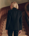 Vintage The Military Blazer in black wool worn by a woman standing before a curved wooden staircase.