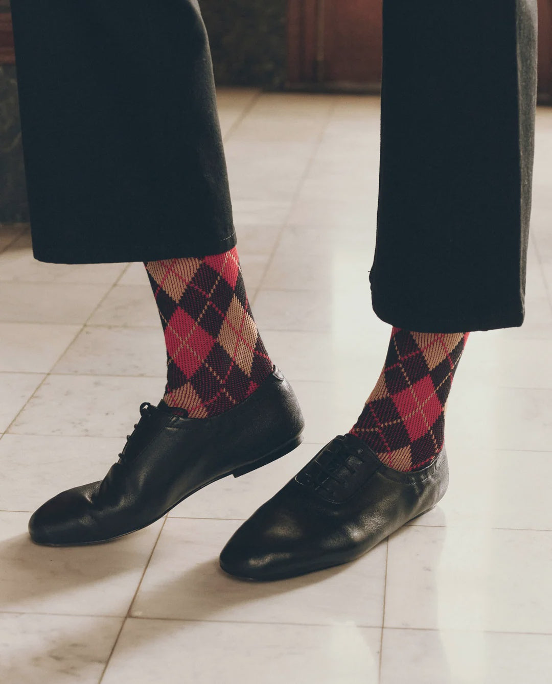 Vintage-style black leather dress shoes paired with red and dark brown argyle socks.