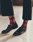 Vintage-style black leather dress shoes paired with red and dark brown argyle socks.