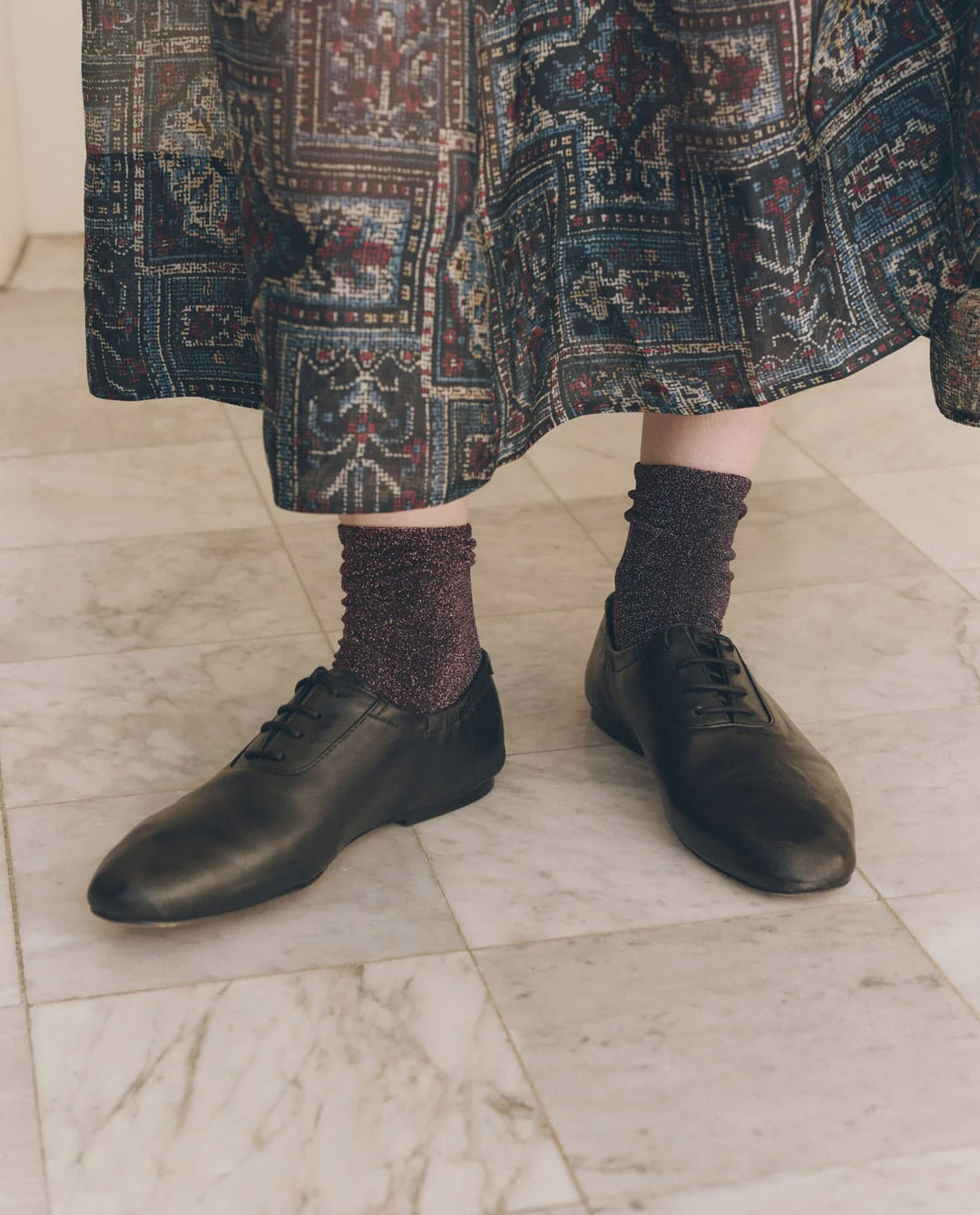 Dark metallic Lurex ankle socks paired with black leather lace-up flats and a patterned midi skirt.