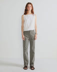 A person with long reddish hair wears Kule’s The Tank, paired with gray straight-leg pants and black sandals, standing against a plain white background.