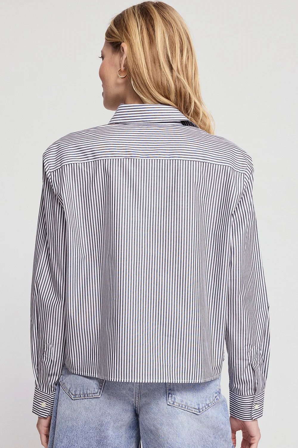 The Shirt LS Boxy Crop top in white with light blue jeans, modern casual style against minimalist backdrop.