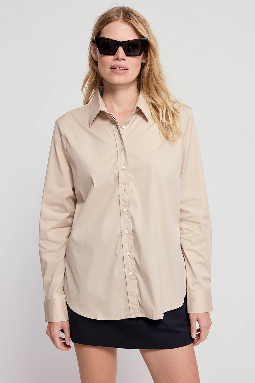 Taupe THE SHIRT The Boyfriend Shirt styled with a black skirt, worn by woman in sunglasses against a light background.