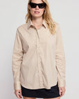 Taupe THE SHIRT The Boyfriend Shirt styled with a black skirt, worn by woman in sunglasses against a light background.