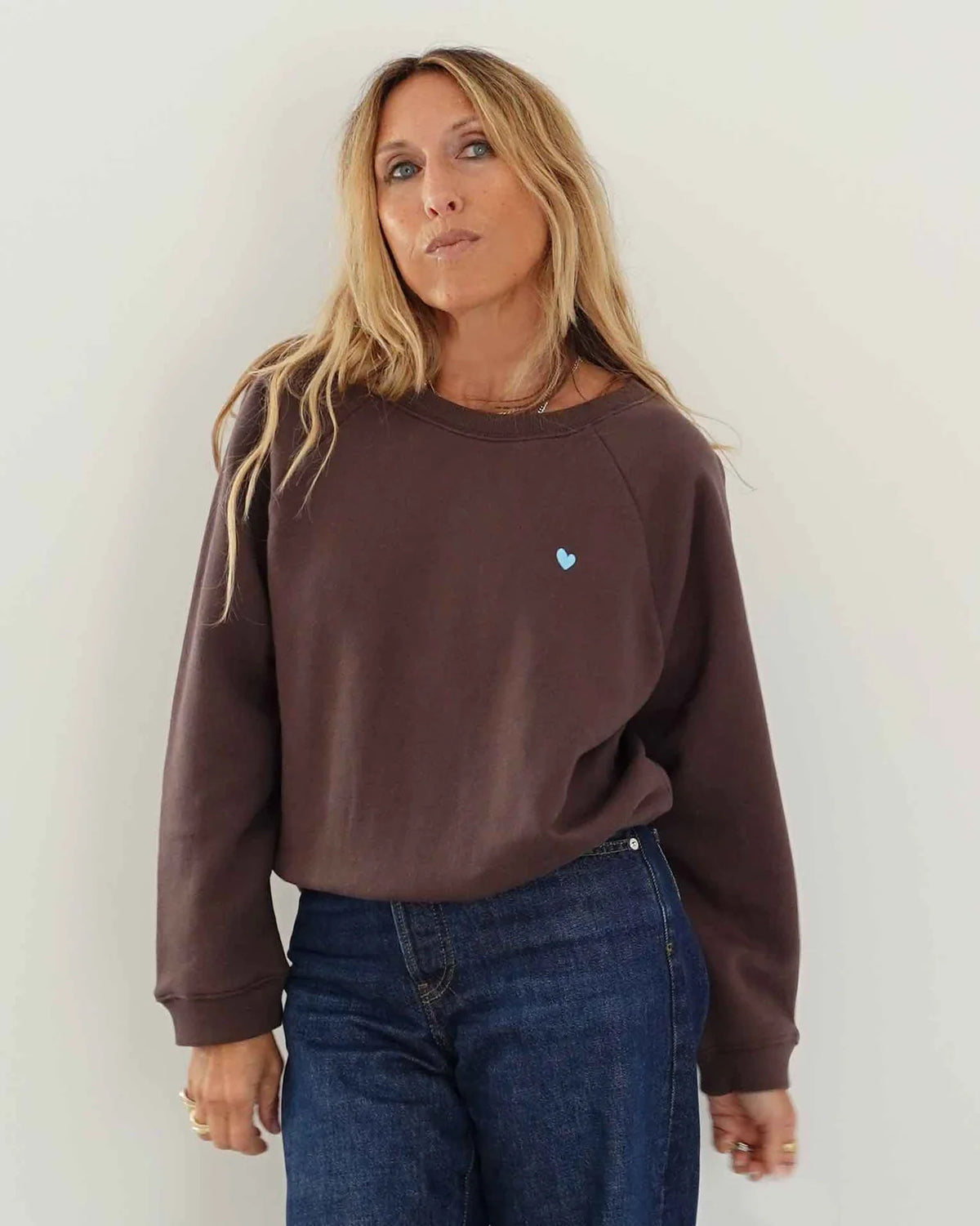 Kerri Rosenthal True Sweatshirt in chocolate brown with blue heart paired with dark blue jeans.