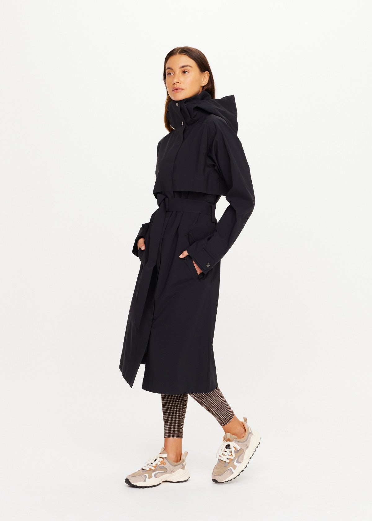 The Upside James Hooded Trench Coat in beige, styled with patterned leggings and sneakers against a white backdrop.