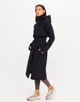 The Upside James Hooded Trench Coat in beige, styled with patterned leggings and sneakers against a white backdrop.