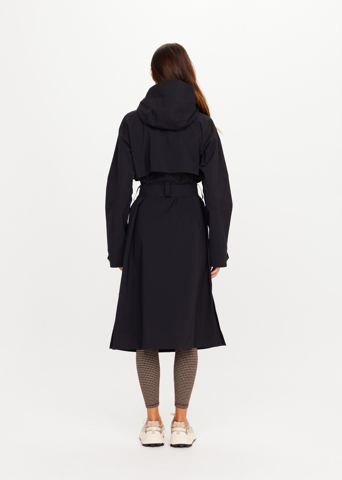 The Upside James Hooded trench coat in black, shown from the back, paired with patterned leggings.