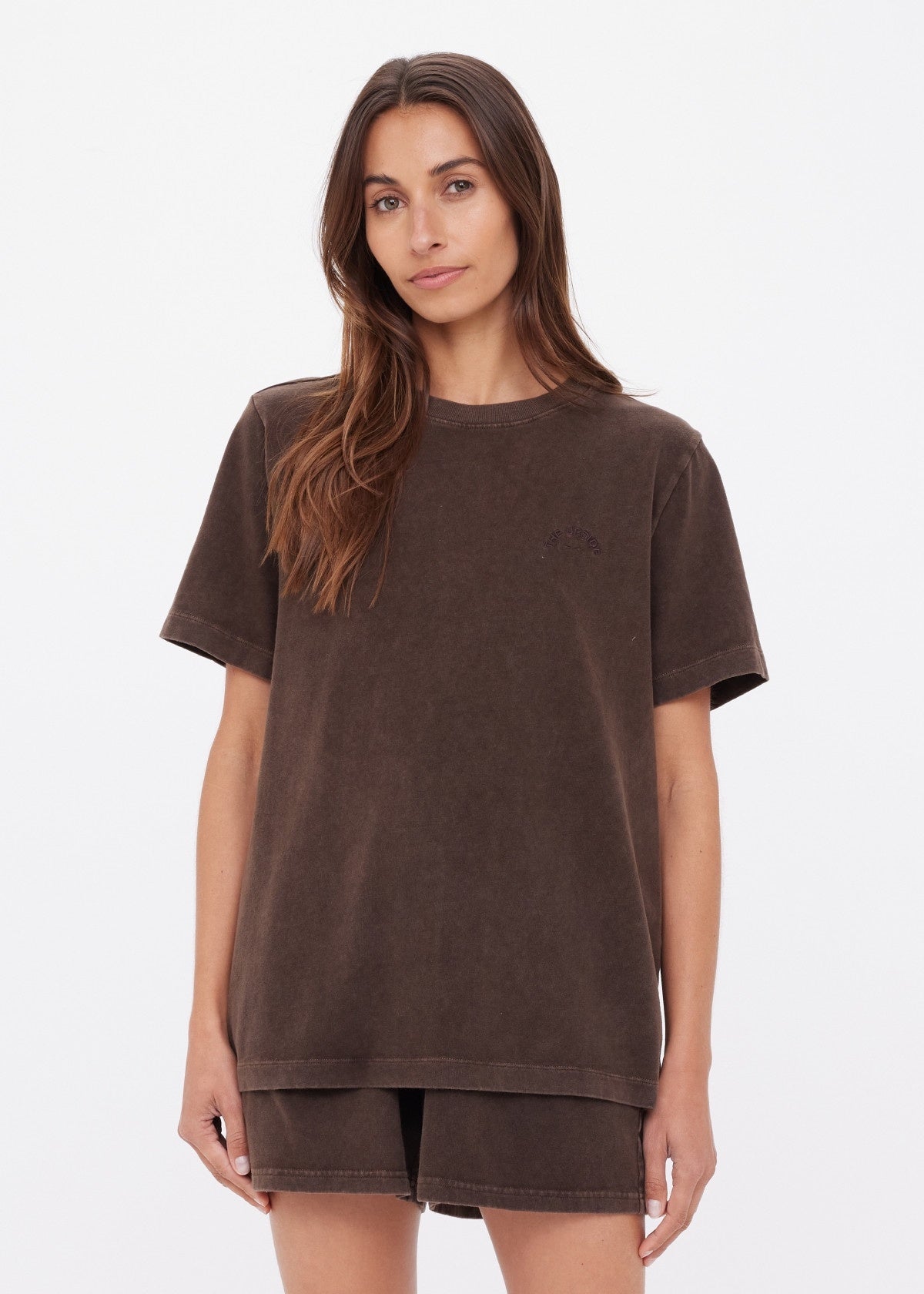 A woman with long brown hair models the SOHO EVA CREW TEE by Citizens Of Humanity/AGOLDE—a loose-fitting, short-sleeved crew neck t-shirt with matching brown shorts—against a plain white background.
