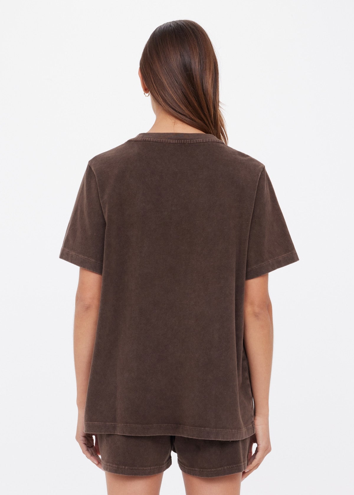 A person with long brown hair wears the SOHO EVA CREW TEE by Citizens Of Humanity/AGOLDE—deep cocoa brown and brushed recycled cotton—with matching shorts, standing against a plain white background, facing away.