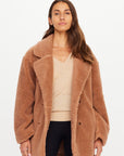 Gracie Teddy Coat in cream faux shearling by The Upside, styled over a beige sweater and black pants, studio backdrop.