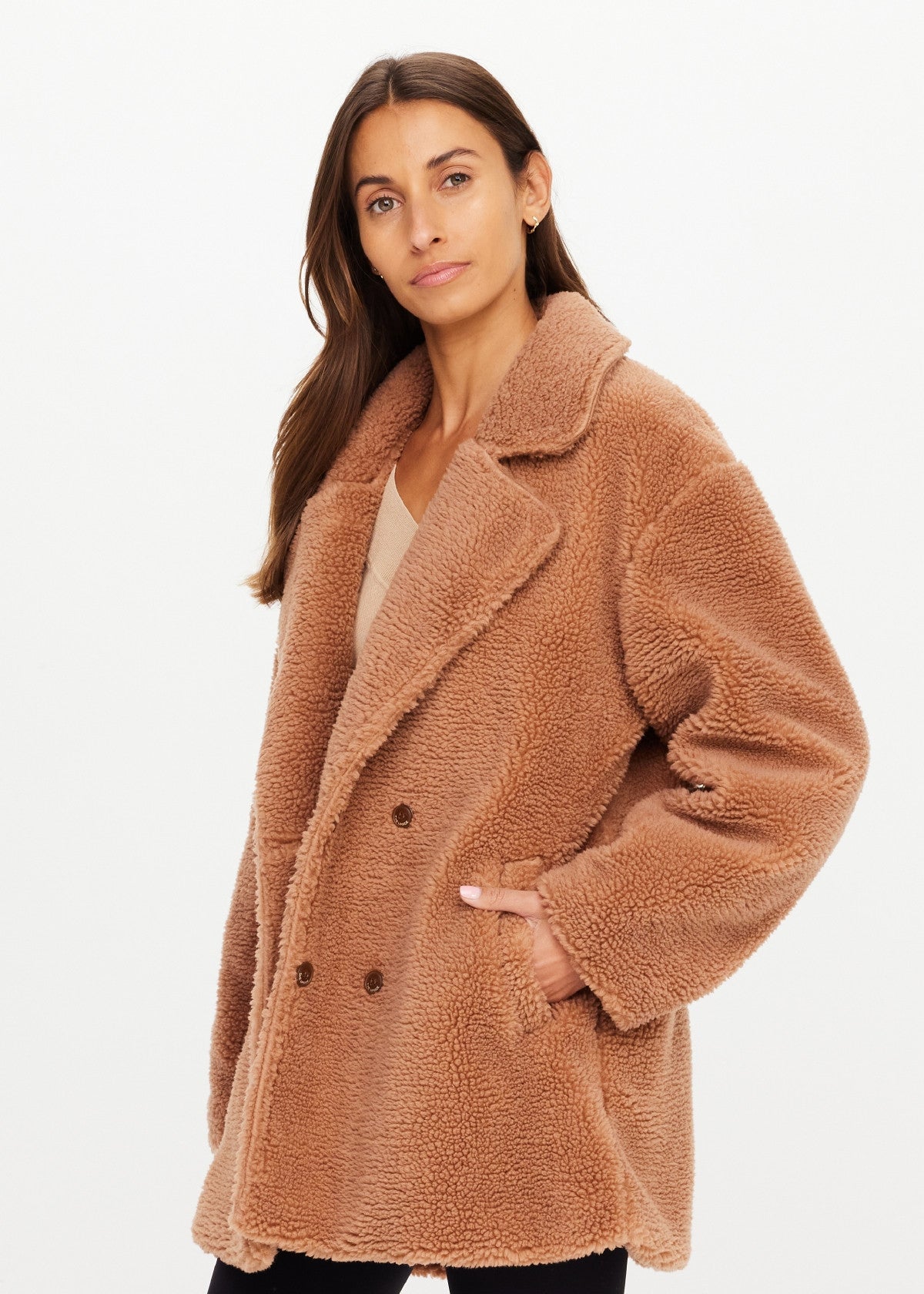 The Upside Gracie Teddy Coat in soft fleece, light color, front pocket detail, styled by model against white backdrop.