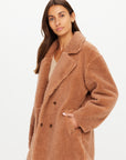 The Upside Gracie Teddy Coat in soft fleece, light color, front pocket detail, styled by model against white backdrop.