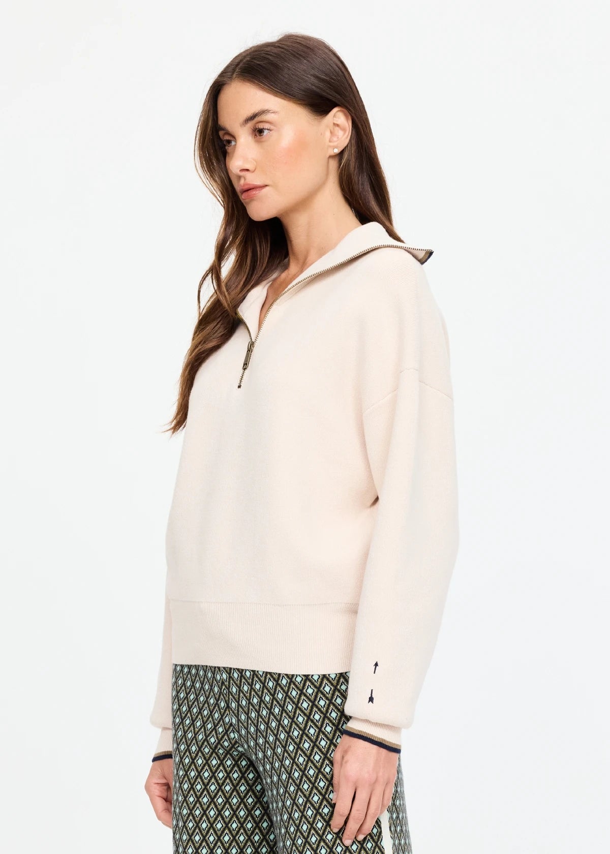 The Upside KAIRO HALF ZIP KNIT sweater and patterned pants in a modern, minimalist setting, side profile view.
