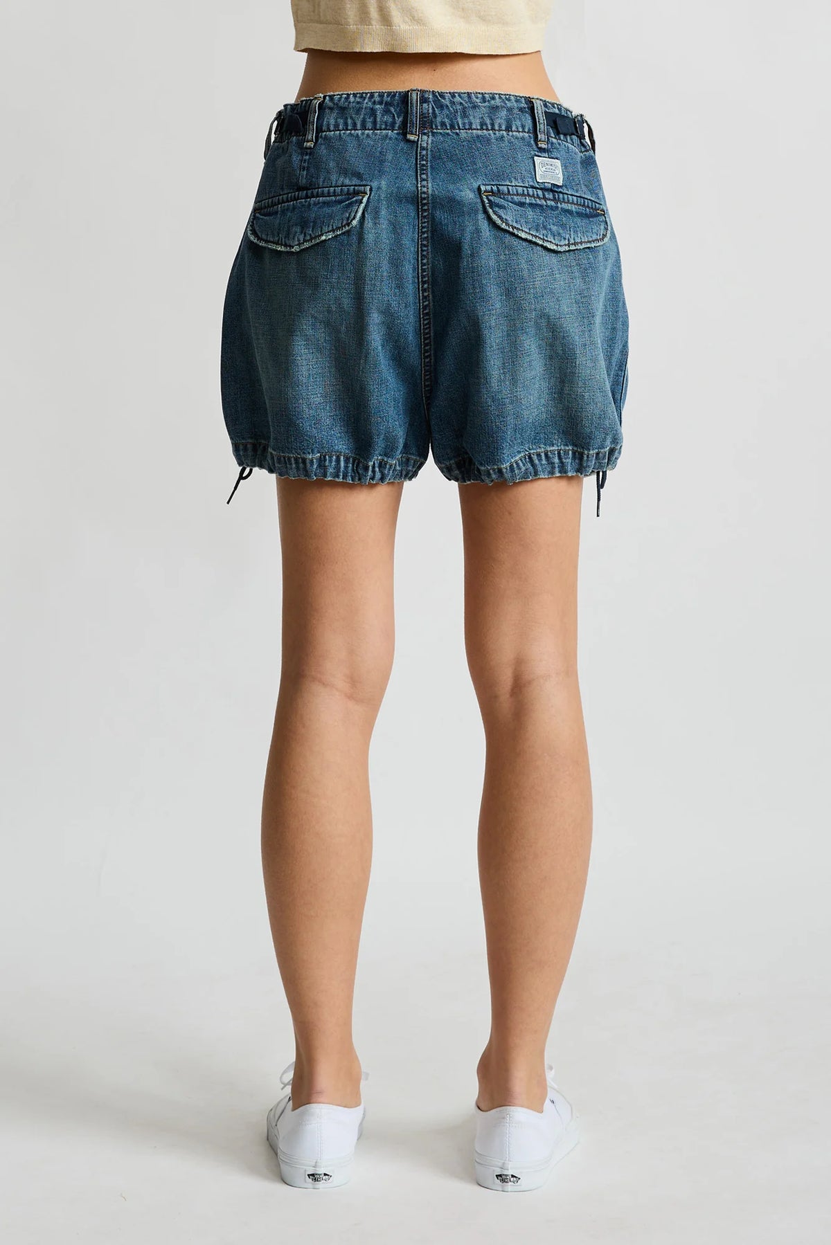 Denimist Utility Short in rigid indigo denim, shown from the back, paired with white shoes on a plain background.