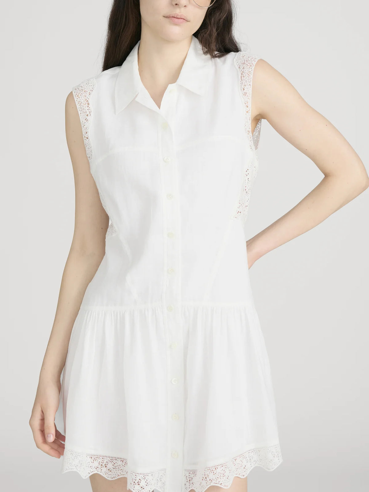 A woman models The Embroidered Day Dress by FRAME, a romantic sleeveless style with lace trim on the shoulders and hem, against a plain light background. Her hair is down and her left hand rests on her hip.