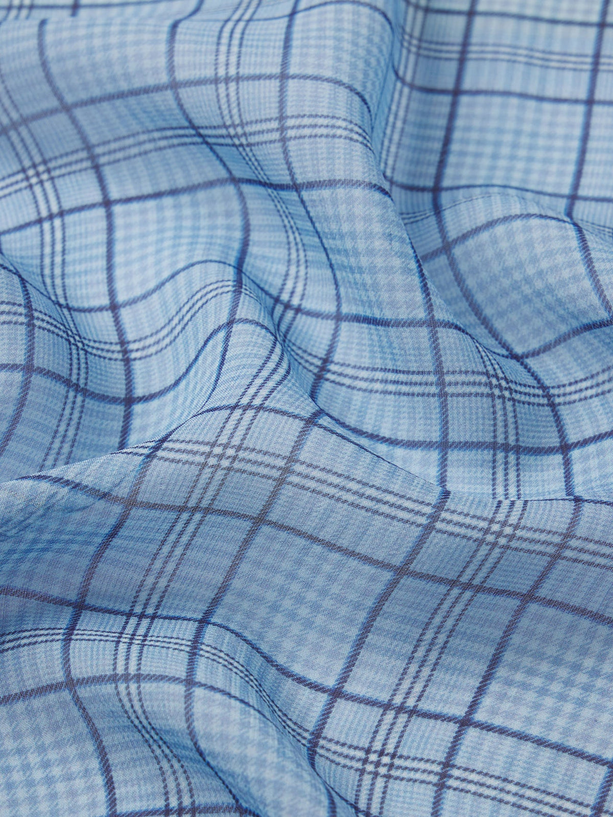 A close-up of soft light blue fabric with a dark blue plaid pattern and gentle folds—ideal for crafting the FRAME Essential Top, adding style and texture to your wardrobe.