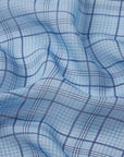 A close-up of soft light blue fabric with a dark blue plaid pattern and gentle folds—ideal for crafting the FRAME Essential Top, adding style and texture to your wardrobe.