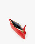 The Clare Vivier Wallet Clutch w/Tabs, made in India, is an elegant small red clutch crafted from Italian nappa leather. It features a zippered top with a gold charm embossed with the logo and opens to reveal a grey interior, set against a plain white backdrop.