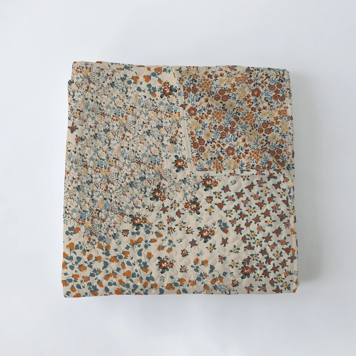 The Winchester Orange Quilt by Faire is a folded Texas-made patchwork quilt with small floral patterns in earthy brown, blue, orange, and beige tones, shown on a plain white background.