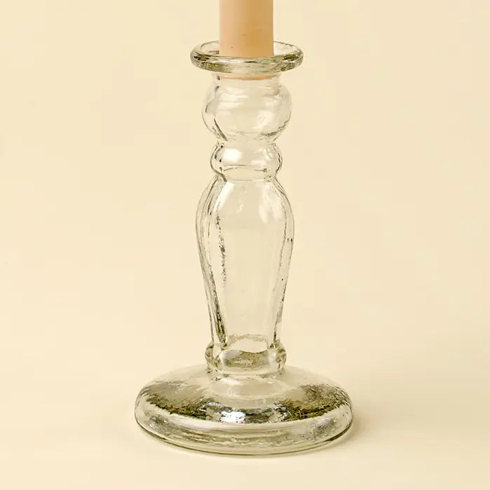 The Vero Glass Candlestick S by Indaba features a clear glass design with a round base, beautifully holding a beige taper candle against a light background for an elegant, timeless look.