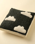 The Indaba Cloudy Day Wall Plaque features three white cloud shapes on a dark square background, ideal as kids' room decor, displayed on a light-colored surface.