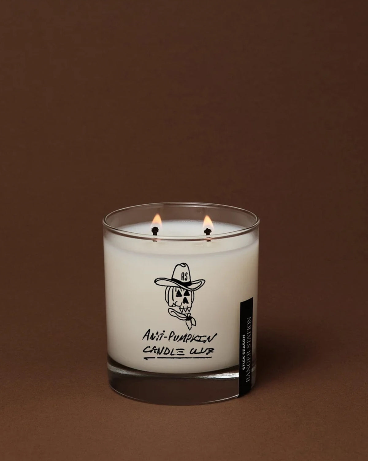 Anti-Pumpkin two-wick candle in a clear glass jar featuring a pumpkin-cowboy illustration from Bungalow.