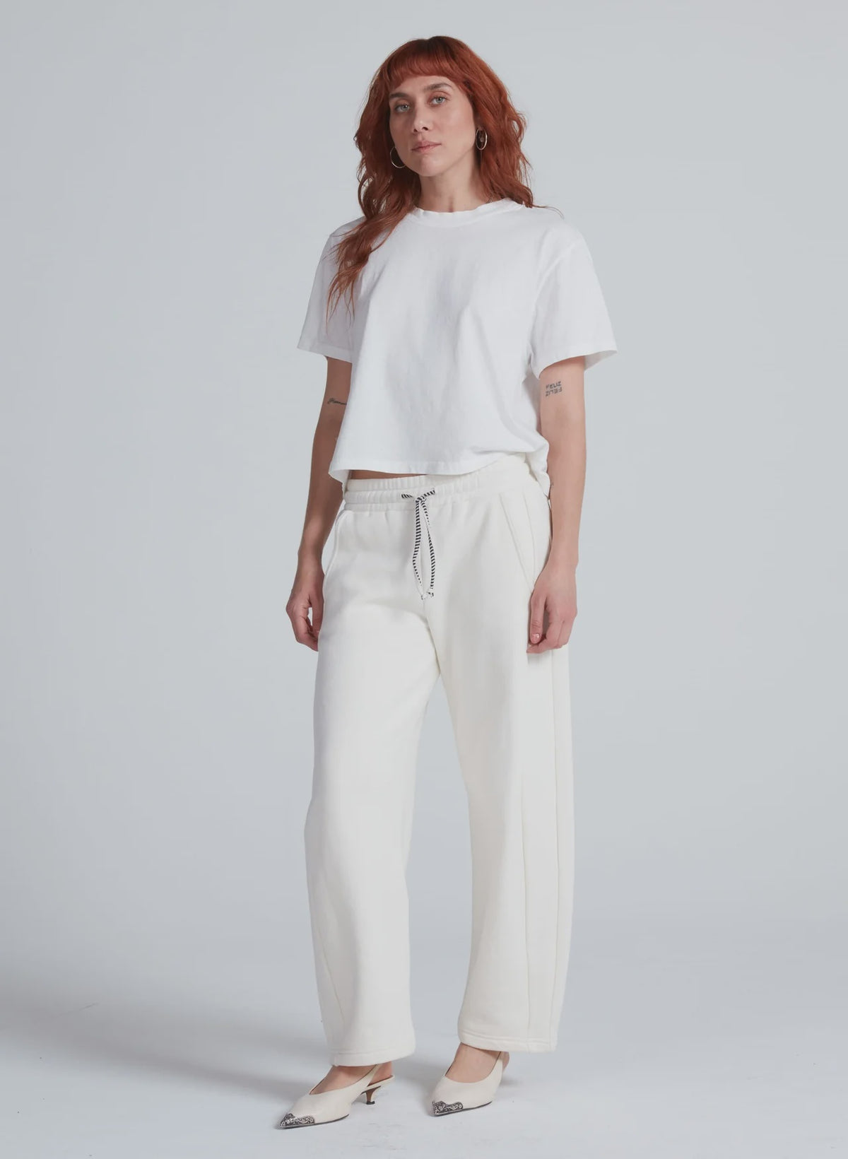 ASKK Cancun relaxed barrel sweatpants in white styled with tee and heels, minimal studio backdrop, modern look.