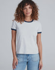 A woman with curly brown hair wears the ASKK Classic Ringer Tee, made from American knit cotton, paired with blue jeans, standing facing forward against a plain light gray background.