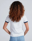 Seen from behind, a person with curly, shoulder-length brown hair wears ASKK's Classic Ringer Tee and blue jeans, standing against a simple light background.