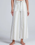 A person stands barefoot in ASKK’s Cropped Sailor pants, featuring high rise, wide legs, large front pockets, and bold white and light beige vertical stripes. The stretch twill adds comfort. Their torso appears partially against a plain light background.