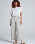 ASKK Cropped Sailor pants in Beach paired with gold sneakers, styled on model with curly hair against gray backdrop.