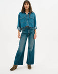 A woman poses against a white background in the ASKK Crosby Flannel, paired with rolled-up sleeves, high-waisted wide-leg jeans, and leopard print ankle boots. Her long brown hair frames her face, completing her chic look.