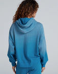 Person with curly hair shown from the back in ASKK's Indigo Dip Dye Hoodie and matching pants, both in a relaxed fit and made from soft American knit cotton, against a plain light background.