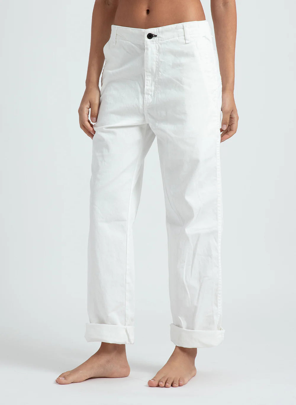 A person wears loose fit, high-waisted ASKK chino twill pants with rolled cuffs in white, standing barefoot against a plain light background.