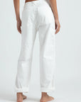 A person stands barefoot on a light-colored floor, facing away from the camera, wearing ASKK's relaxed-fit chino twill pants with rolled cuffs and back pockets for comfort.