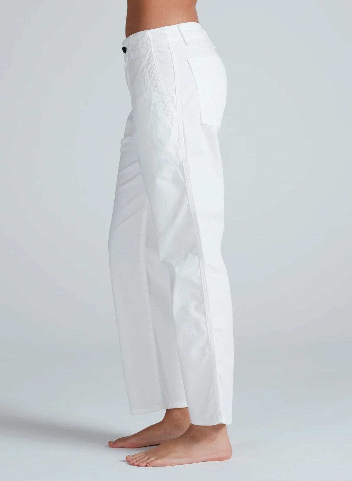 A person stands barefoot on a light background, shown from the side wearing ASKK Tomboy Twill white high-waisted, straight fit pants with a side pocket.