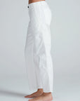 A person stands barefoot on a light background, shown from the side wearing ASKK Tomboy Twill white high-waisted, straight fit pants with a side pocket.