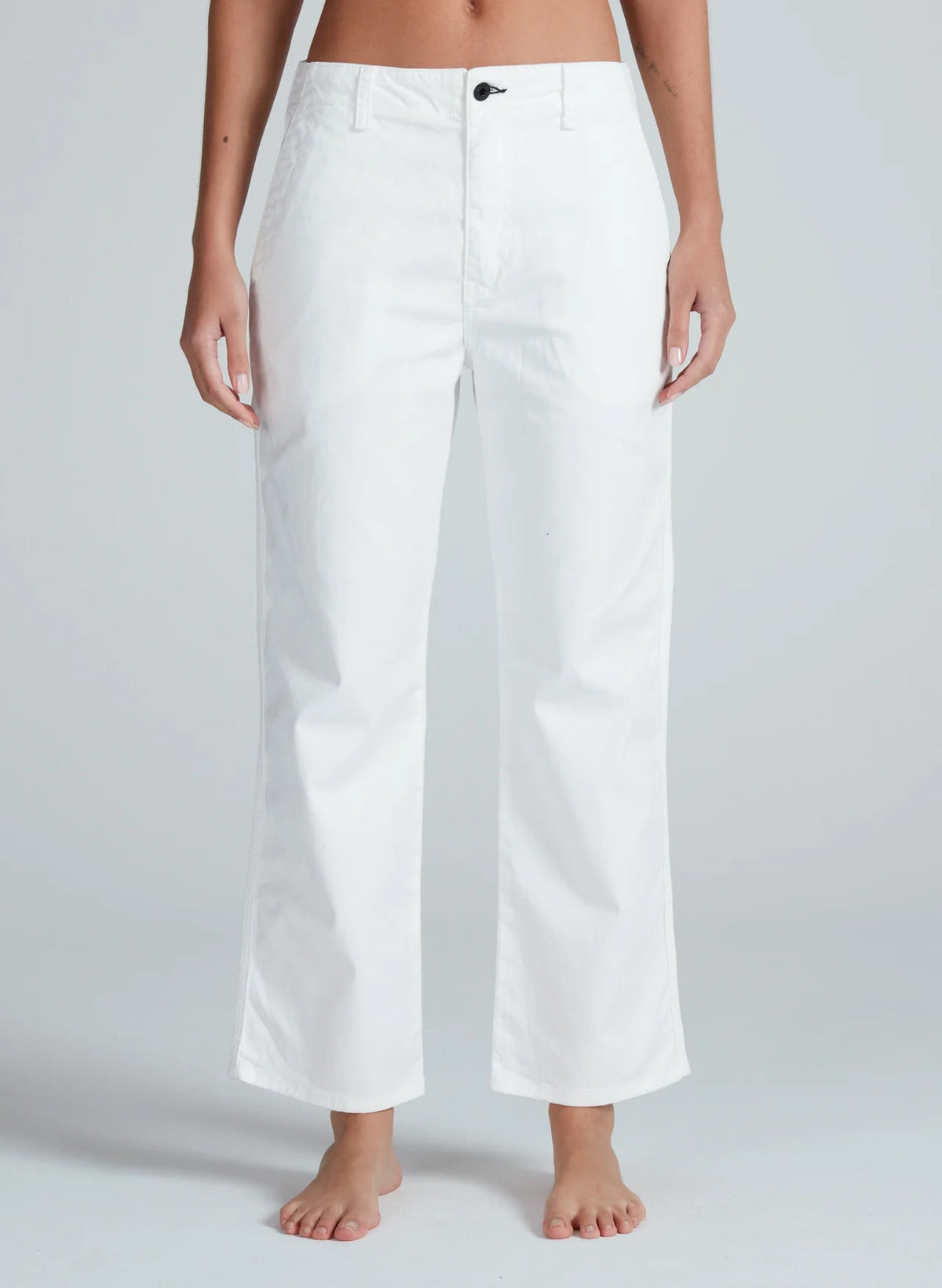 A person models the ASKK Tomboy Twill high-waisted, straight fit white pants, barefoot against a light gray background, showing only their lower torso and legs.