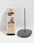 A box of Faire Low Smoke Incense stands next to a lit stick in a smooth gray stone holder against a white background. The beige packaging features stone graphics and product details.