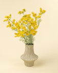 The Indaba Queen Anne Lace Spray Yellow features delicate faux flowers with thin green stems, displayed in a cream ceramic vase with vertical grooves—perfect accent decor for pale, solid backgrounds.