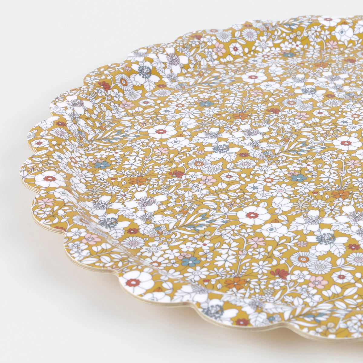 The Meri Meri x Liberty June's Meadow Small Tray by Faire features a decorative scalloped edge and detailed floral pattern in white, gold, blue, and red on mustard yellow, photographed against a plain white background.