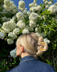 Faire Lucky Horseshoe Hair Clip on blonde hair, styled outdoors among blooming white flowers and green foliage.