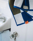The Typical Navy/Moss Stripe Bath Towel, featuring blue, white, and olive stripes with an orange tag, hangs over a white door with a glass knob; part of a white sink appears in the background.